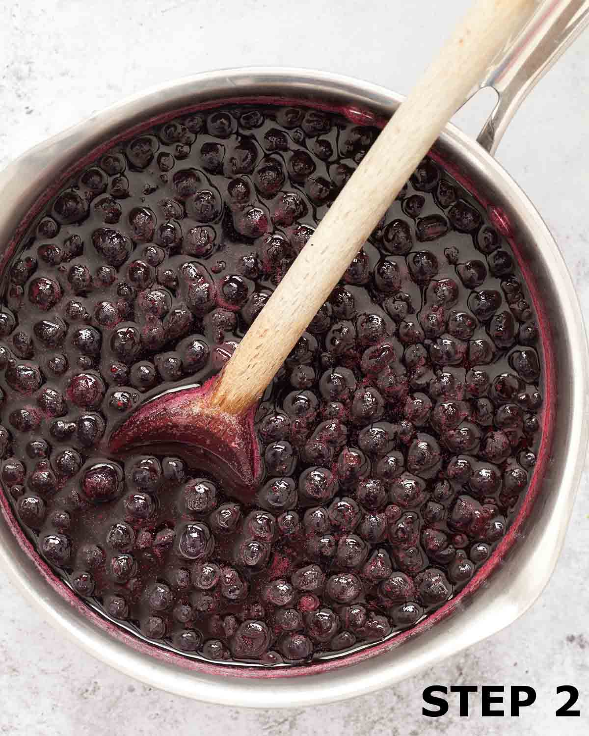Blackcurrant sauce in a pan with a wooden spoon.
