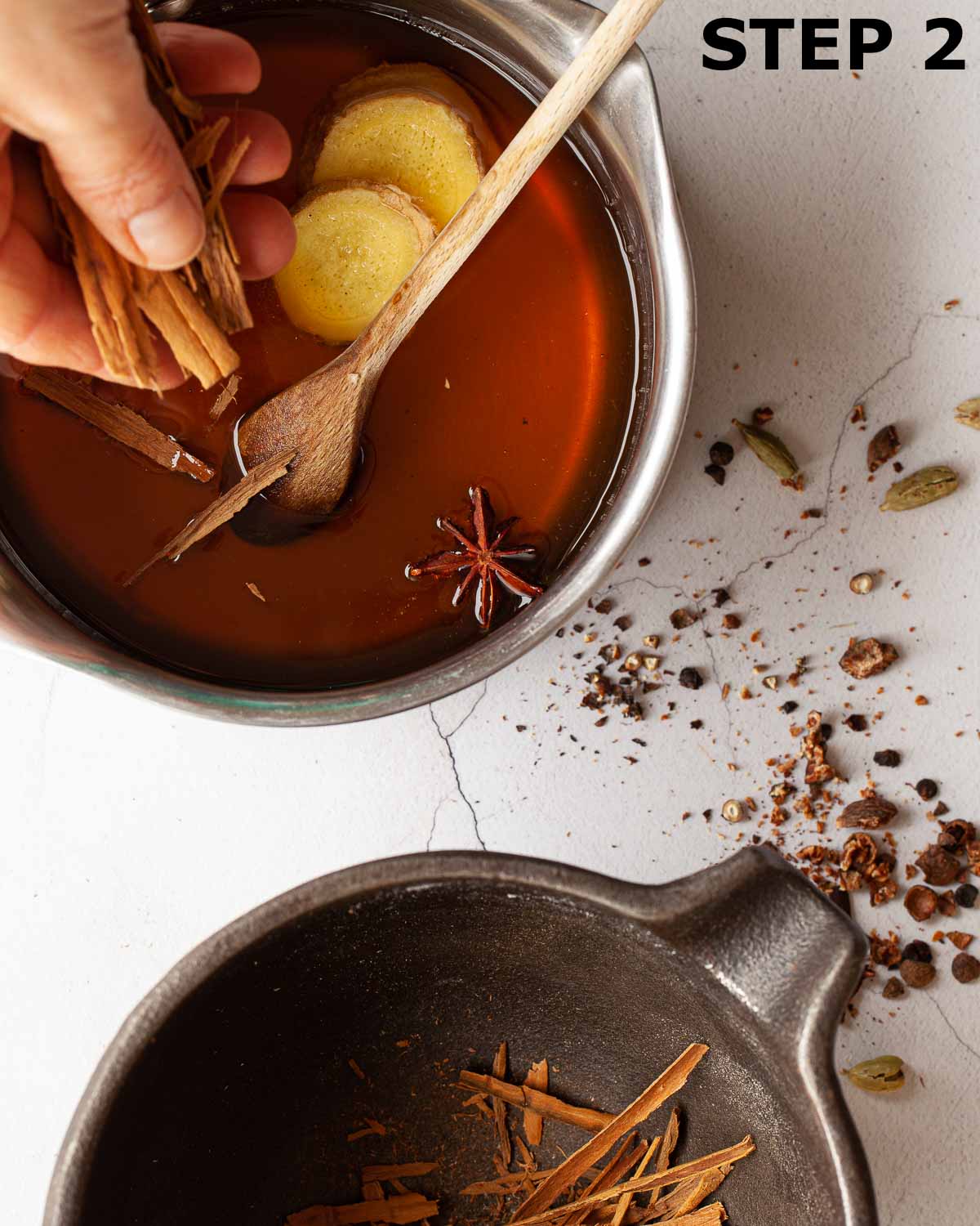 A person adding spices to a pan of warm simple syrup.
