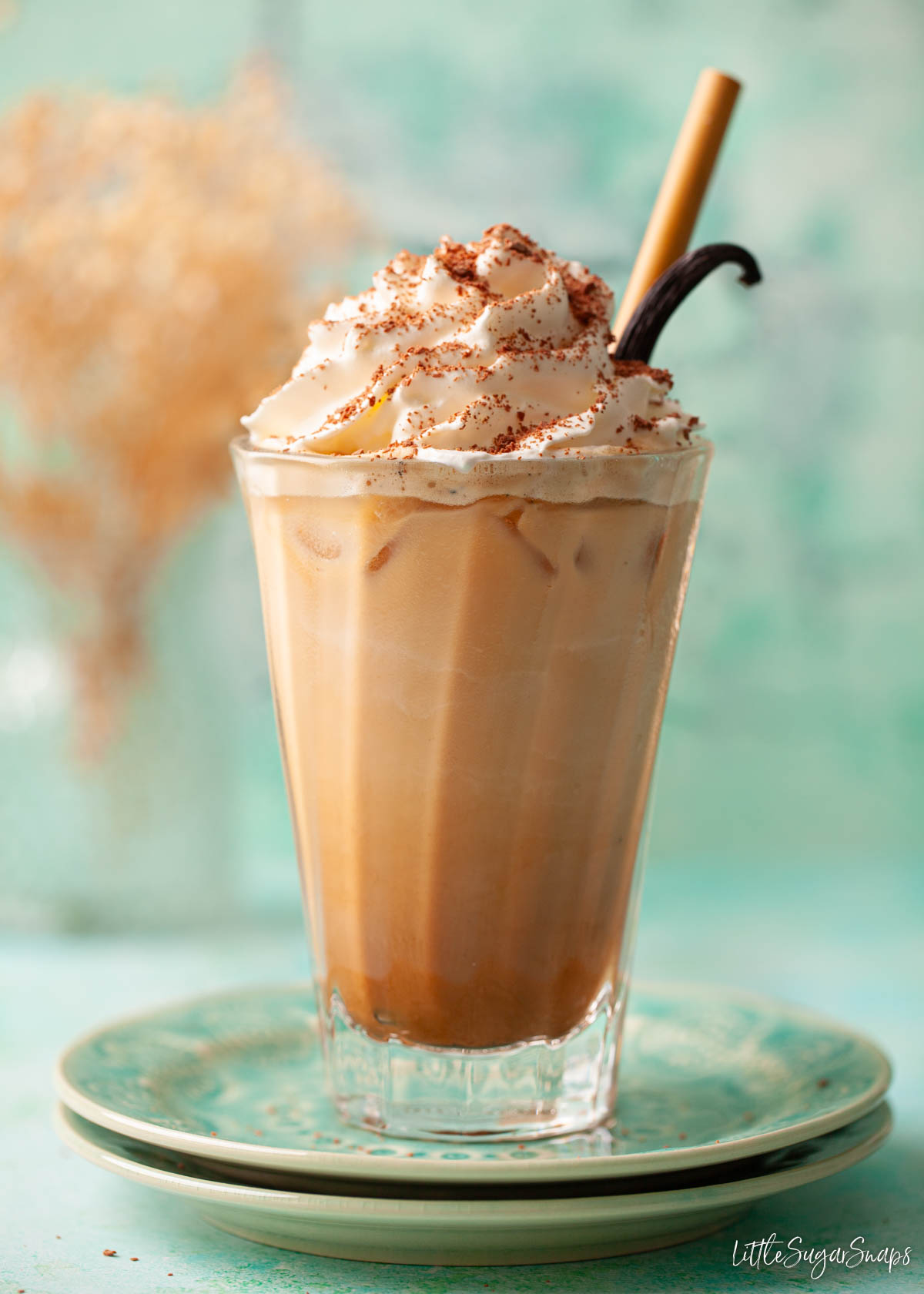 A glass of iced vanilla bean latte topped with whipped cream, chocolate and vanilla pod.