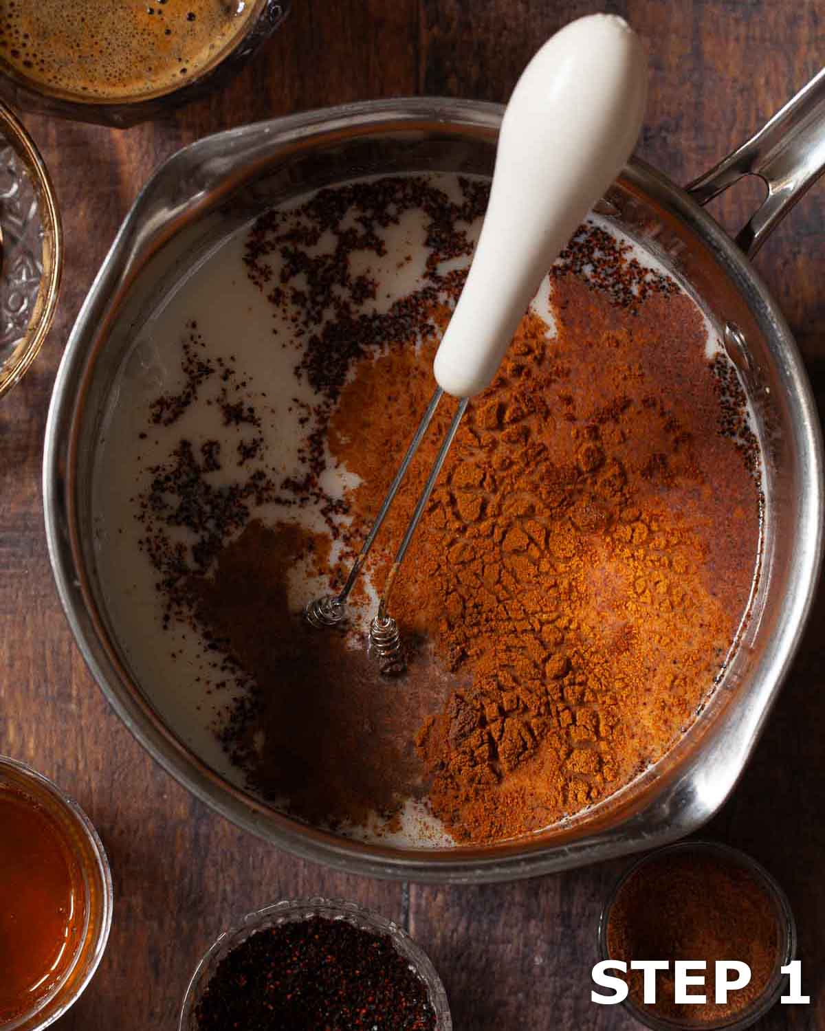 Cocoa powder and ground spices in a small saucepan with cold milk and a handheld whisk.