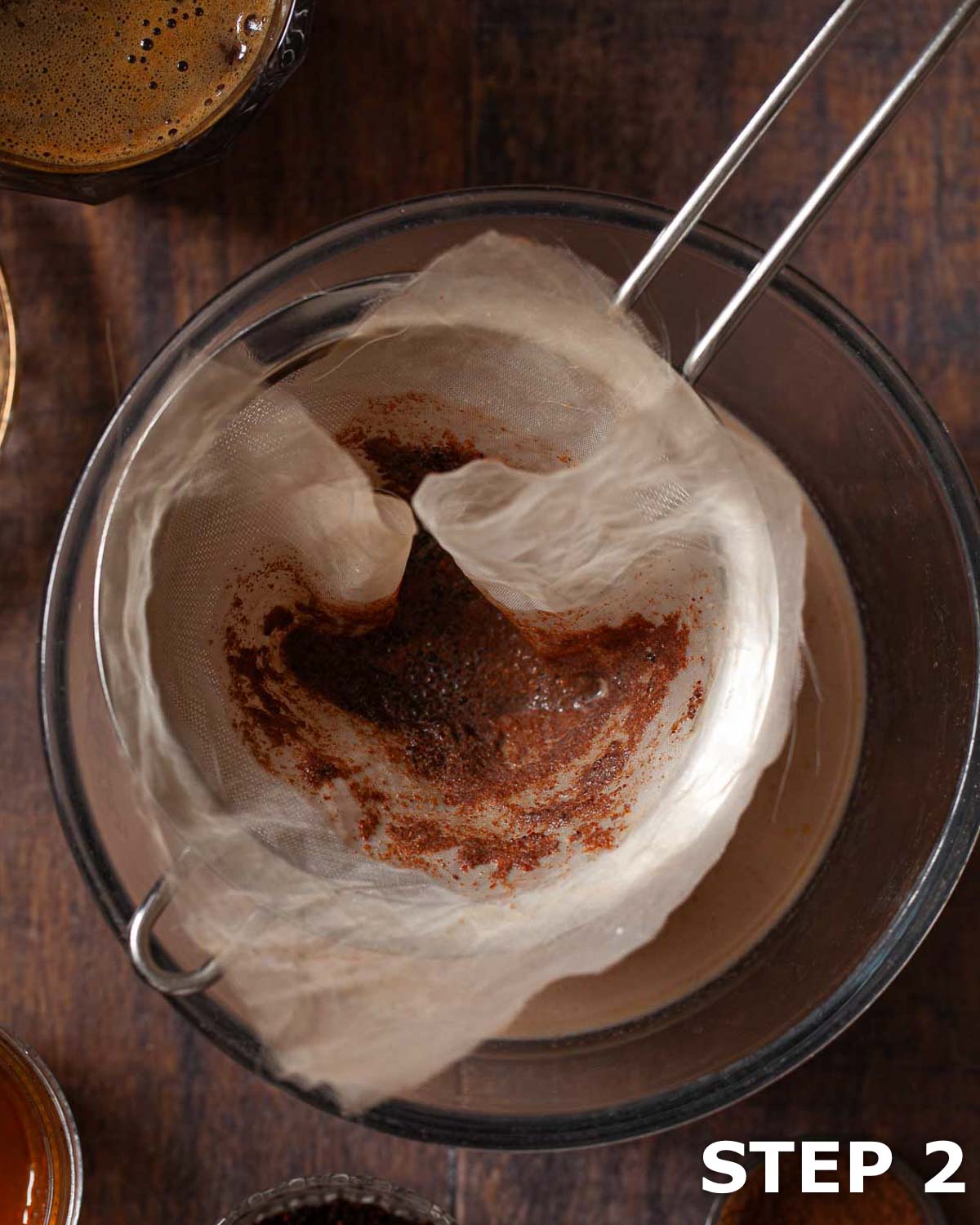 Ground spices being strained out of chocolate milk through a sieve and cloth.