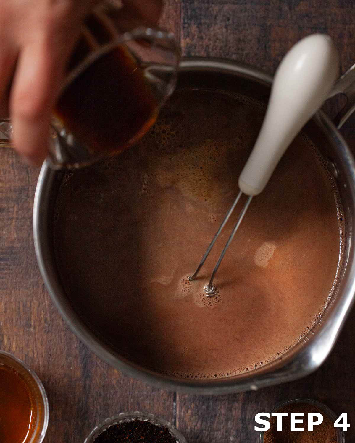 A person pouring espresso into spiced infused chocolate milk in a pan.
