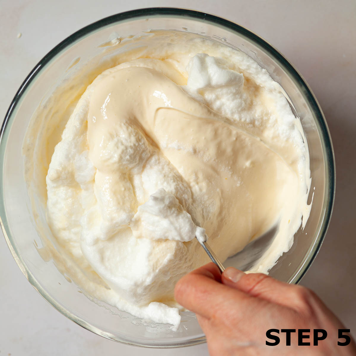 A person folding whipped egg white into tiramisu filling.