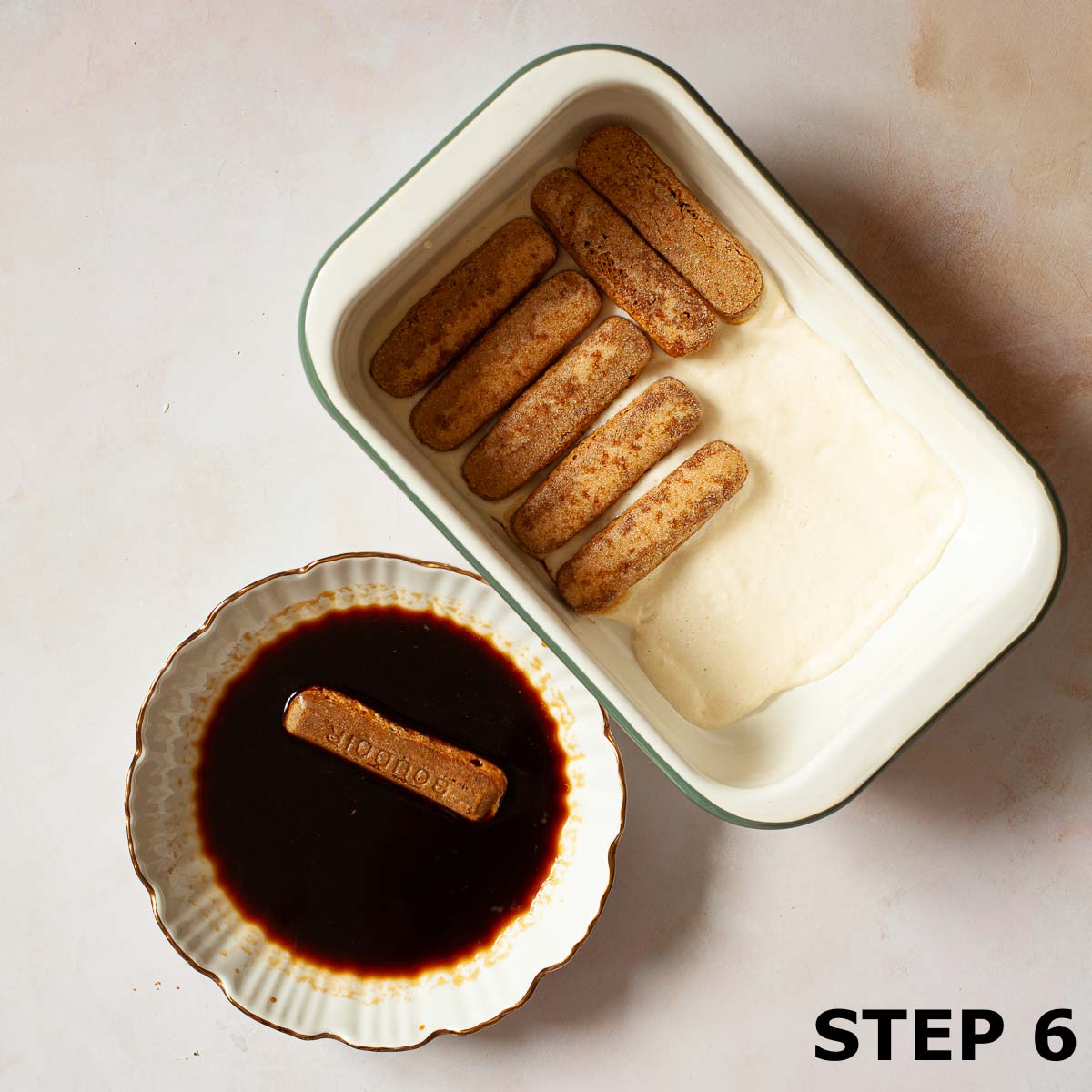 Coffee-soaked ladyfingers being layered into a creamy dessert.
