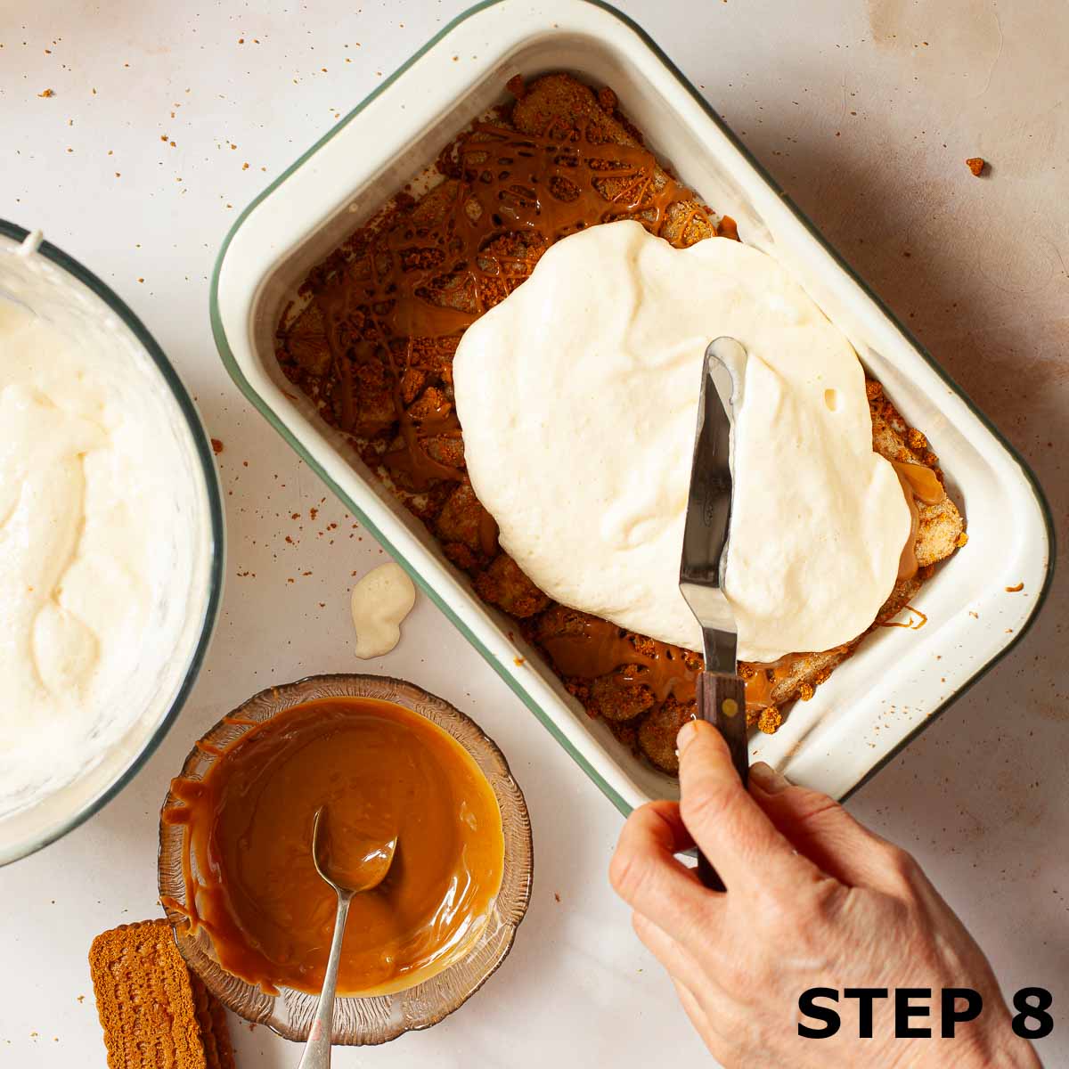 A person spreading mascarpone filling over Biscoff tiramisu.