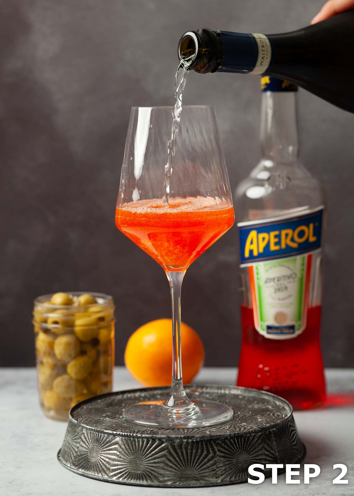 A person pouring prosecco into a glass with Aperol in it.