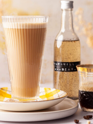 Glass of vanilla bean latte with a bottle of syrup and espresso coffee next to it.
