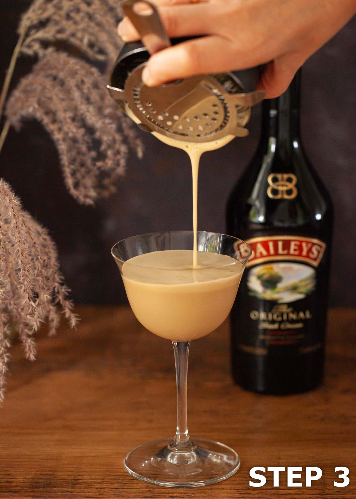 A person straining a Baileys espresso martini cocktail into a serving glass.