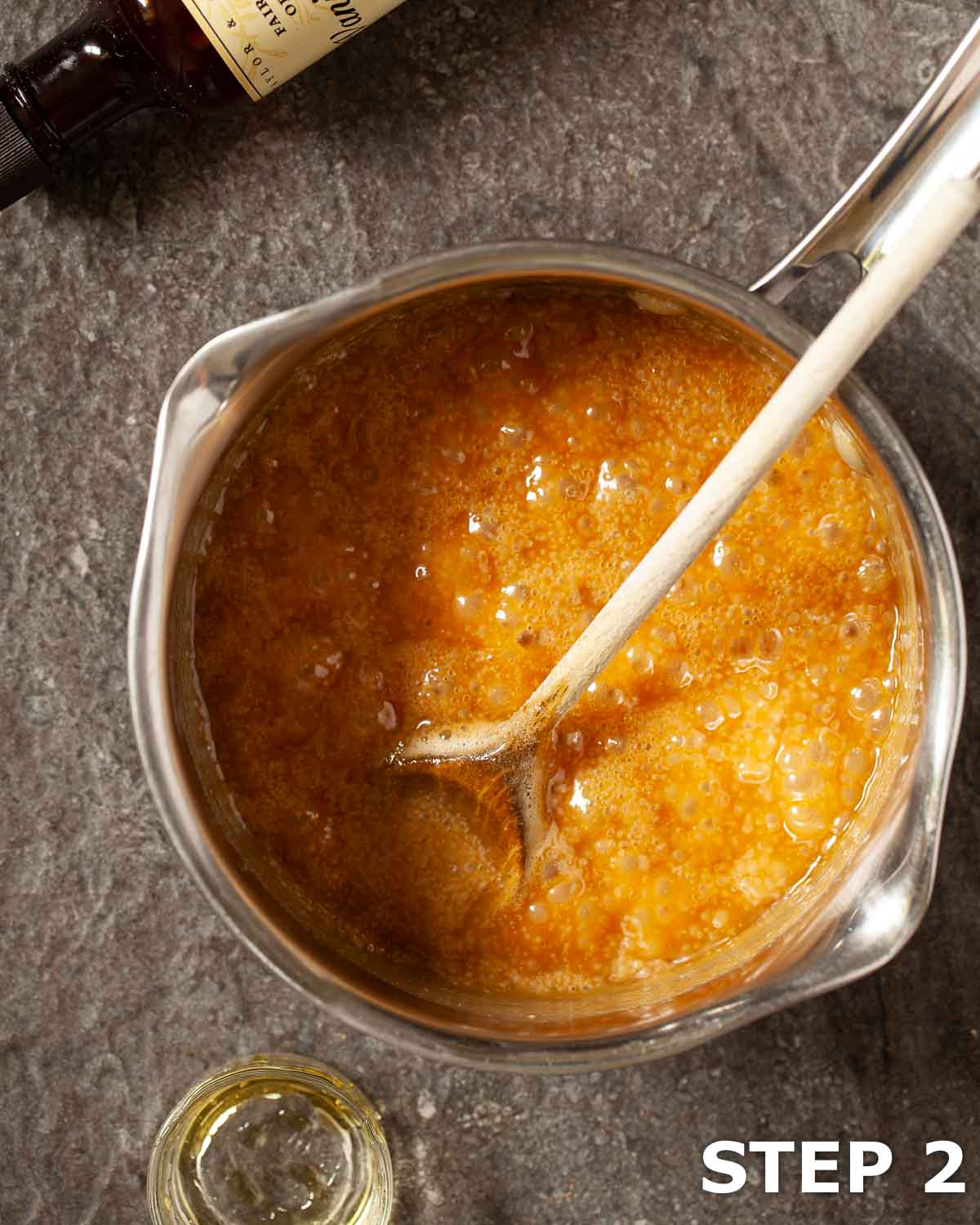 Freshly cooked butterscotch sauce bubbling in a pan with a wooden spoon in it.