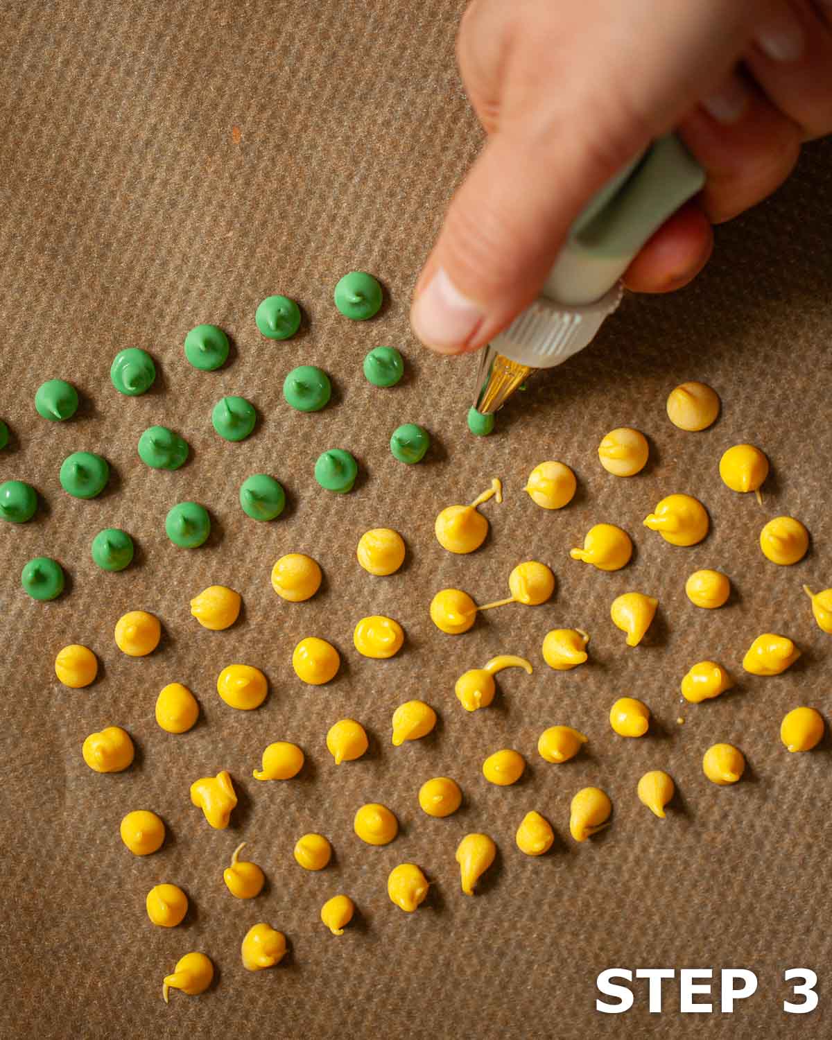 Coloured candy melts being piping into small dots on baking parchment.