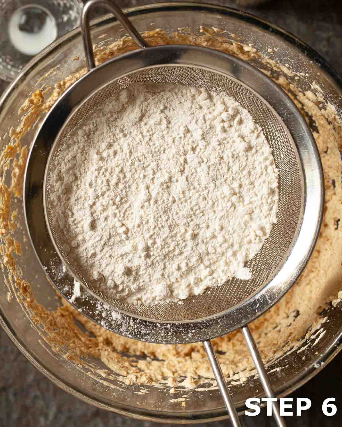 Flour being sieved into cake batter in a mixing bowl.