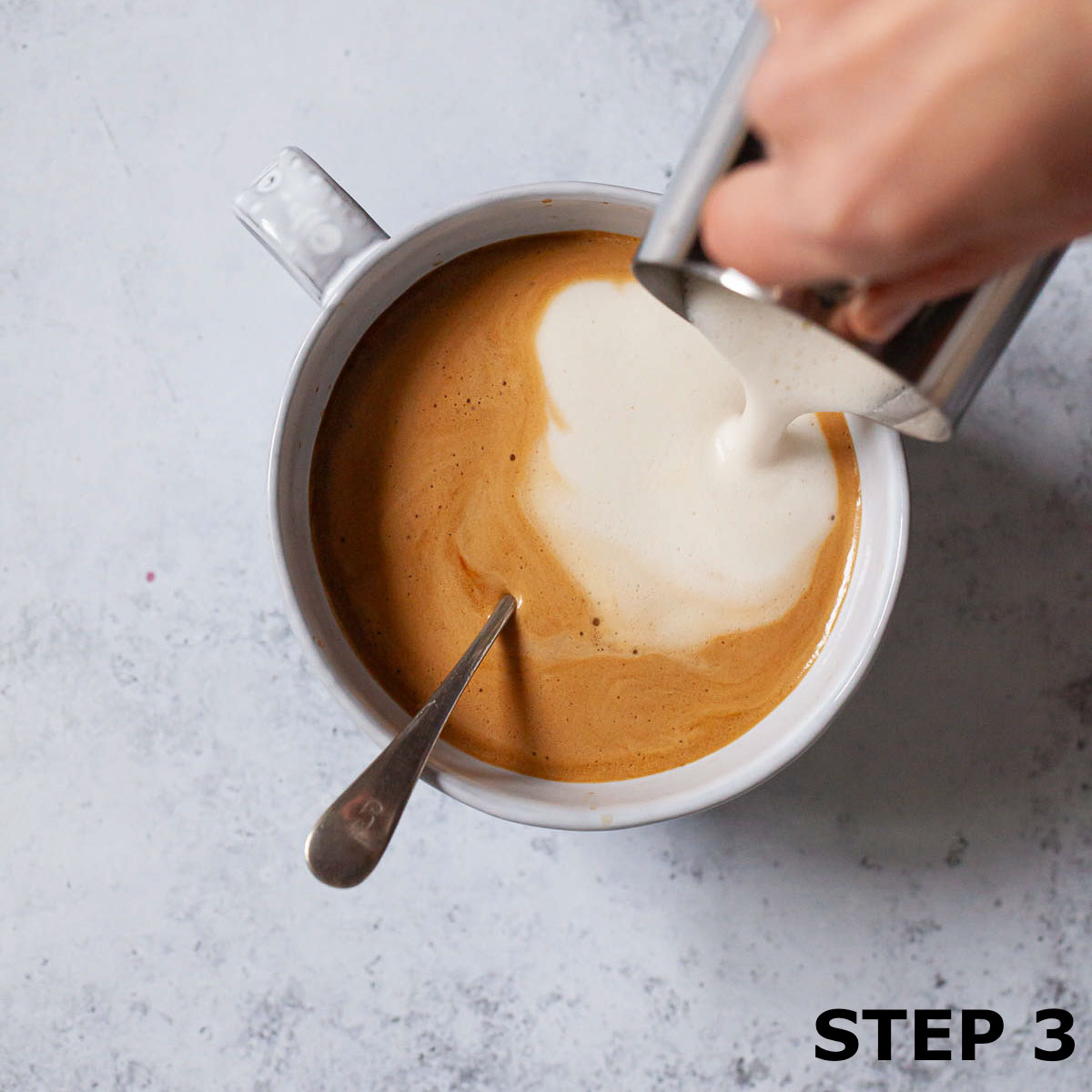 Person pouring steramed milk into coffee to make oat milk latte.