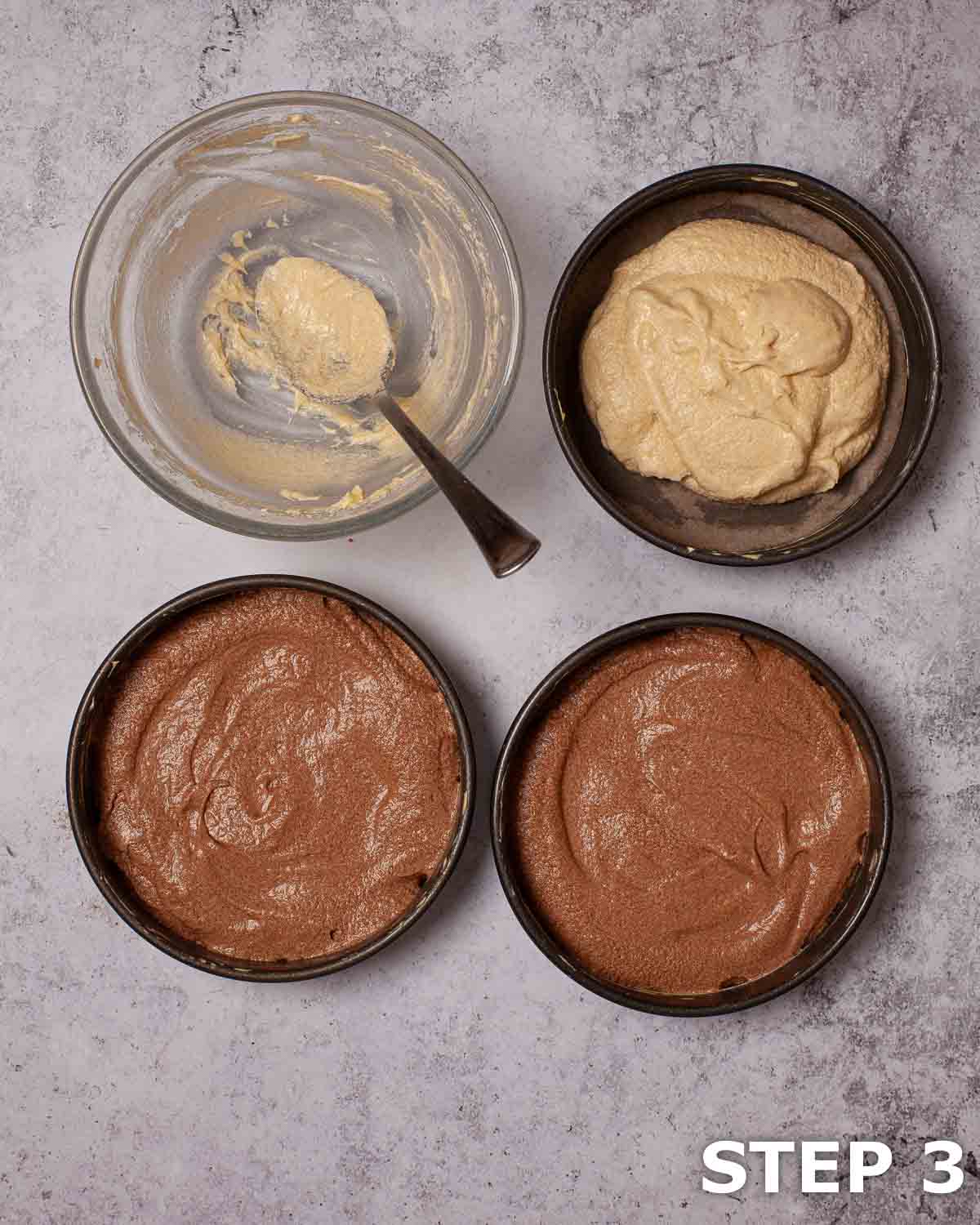 Chocolate and vanilla cake batter in three baking tins with an empty mixing bowl alongside.