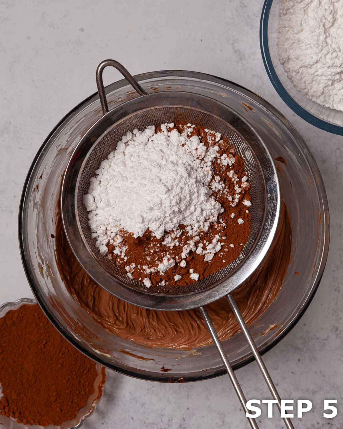 Cocoa and icing sugar in a sieve over a bowl of Nutella buttercream.