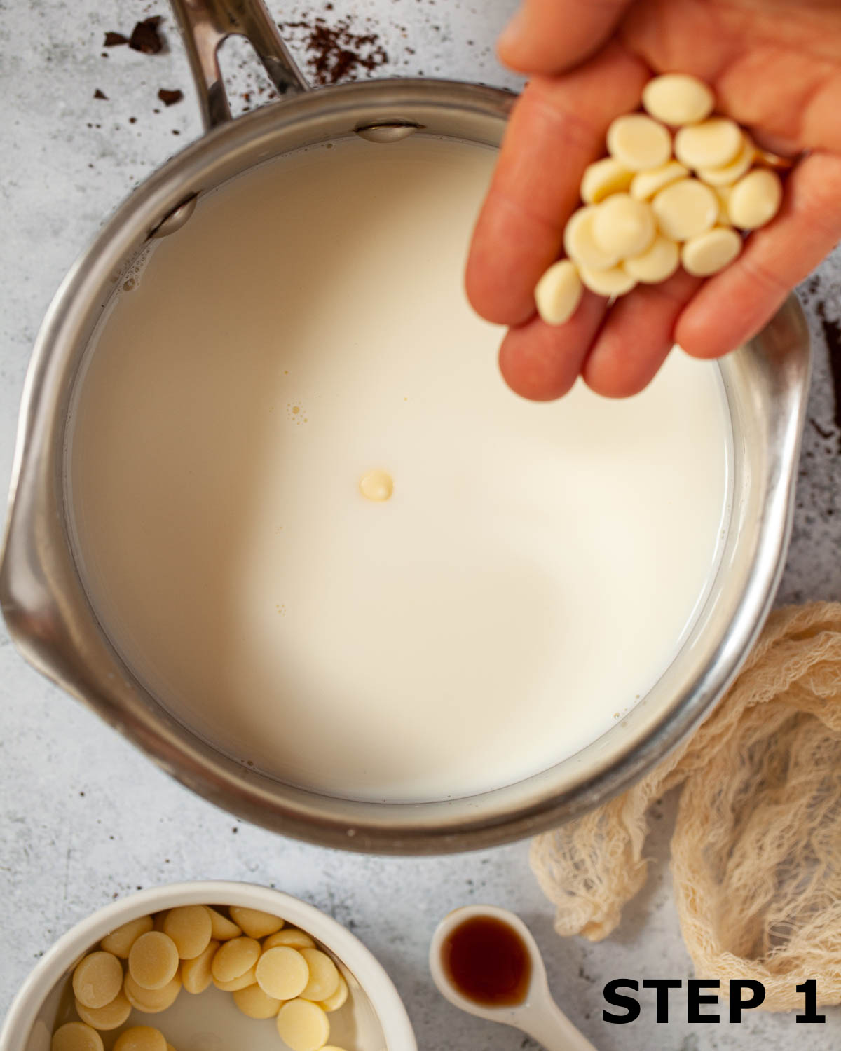 A person adding white chocolate chips to hot milk in a pan.