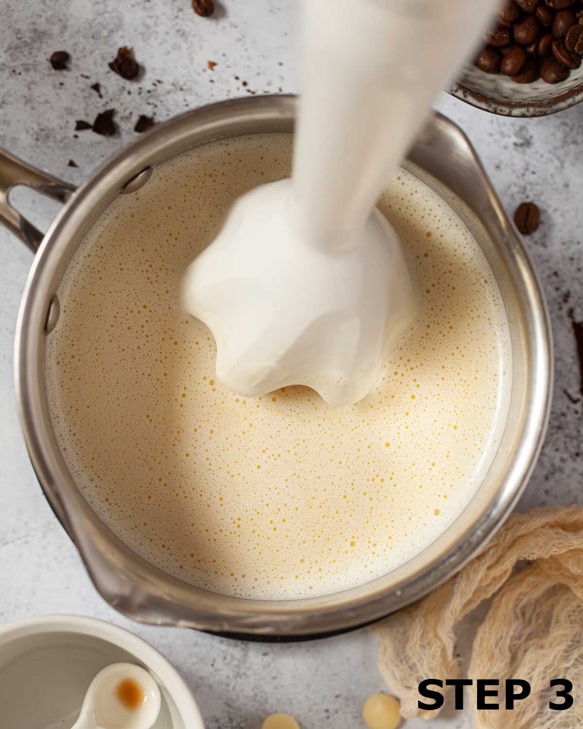 Emersion blender in a pan of frothed white chocolate milk.