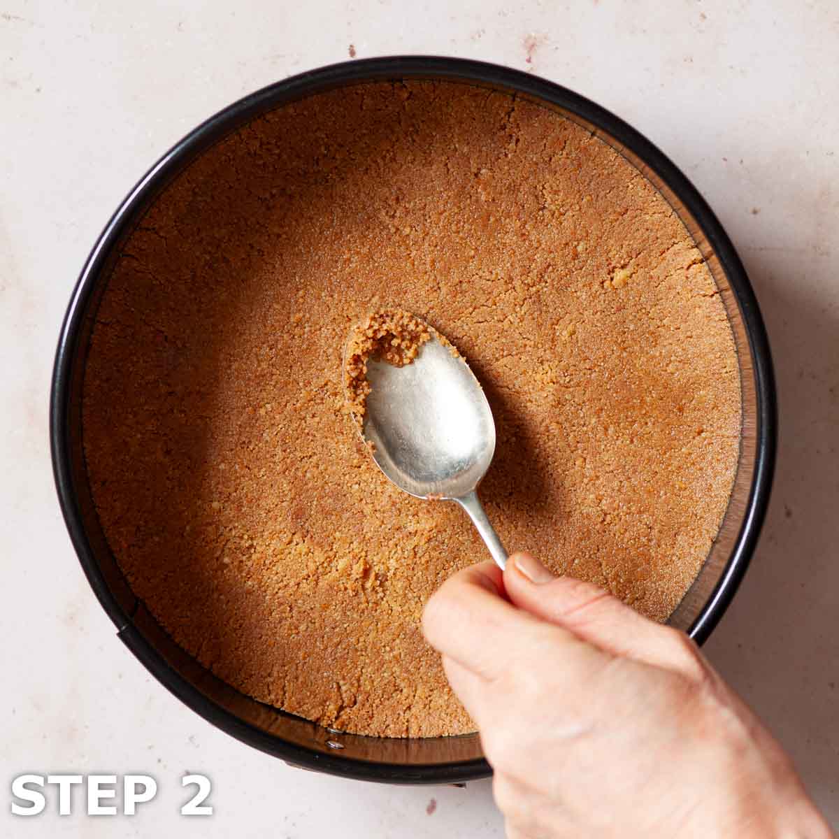 A person pressing the biscuit base of a cheesecake into a baking tin.
