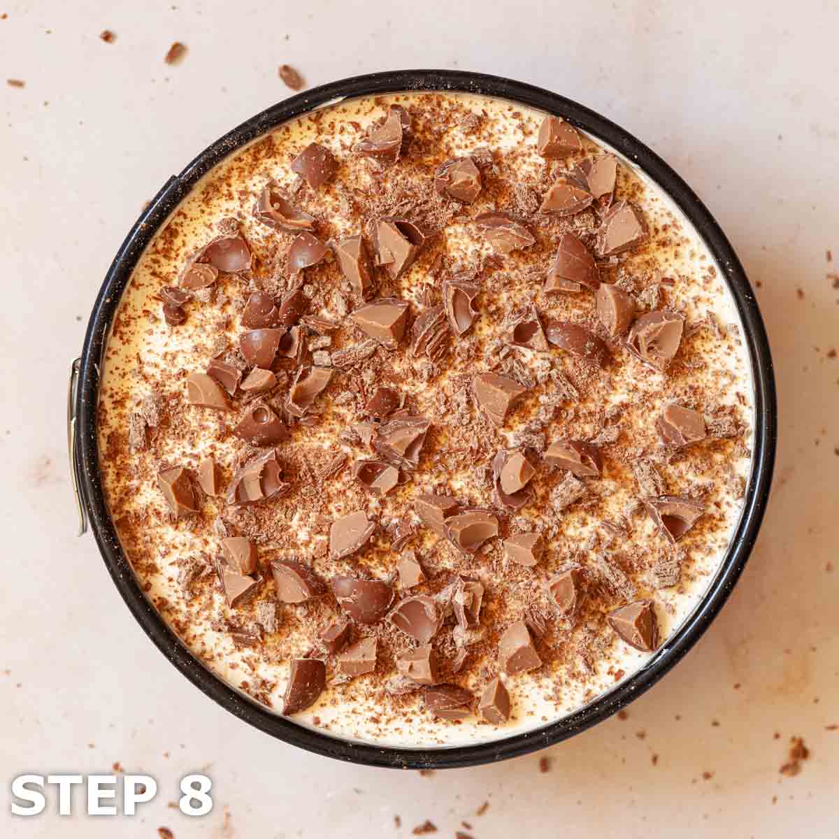 Cheesecake in a baking tin topped with chocolate pieces.