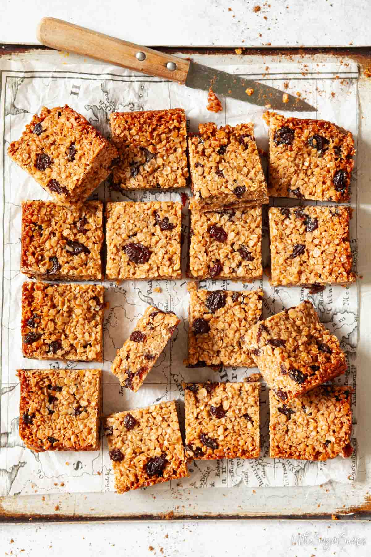 Fruity flapjack with raisins cut into squares with a knife at the side.