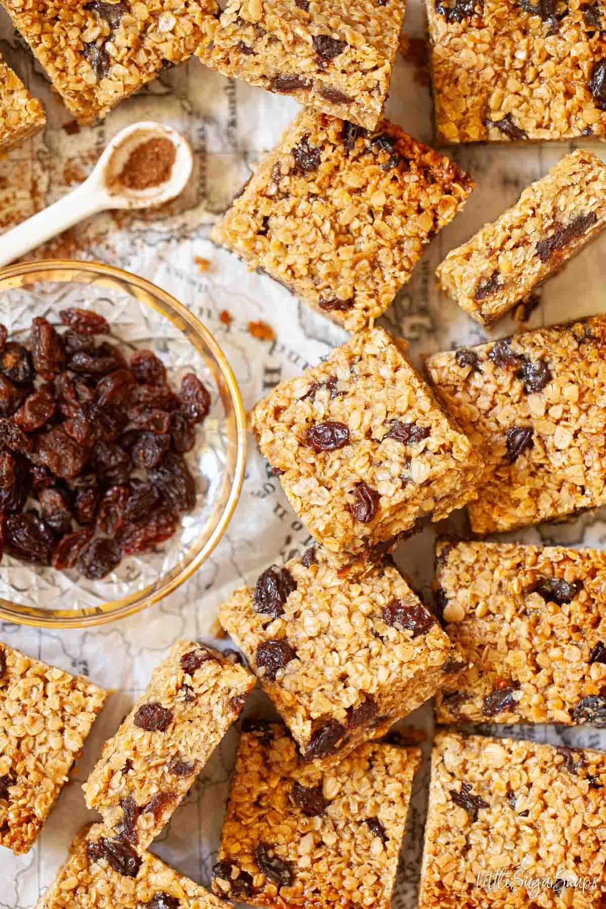 Squares of fruit flapjack with a plate of raisins next to them.