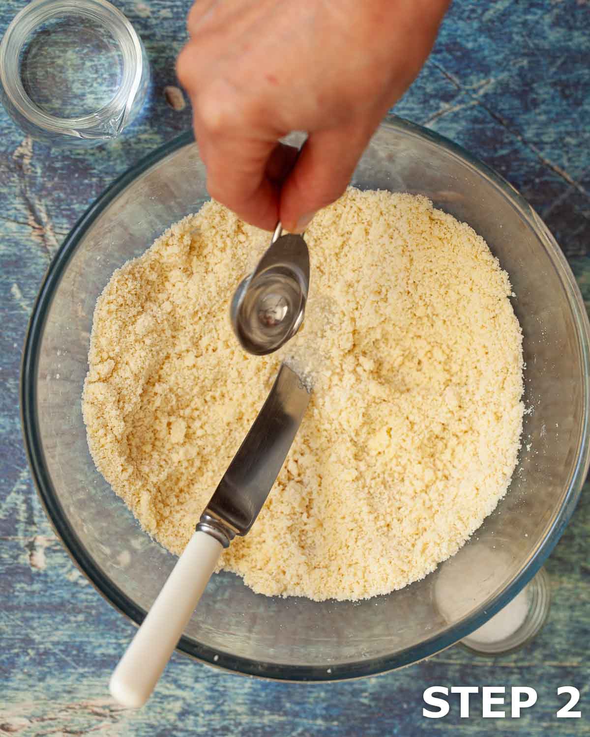 Person adding water to flour and butter to make shortcrust pastry dough.