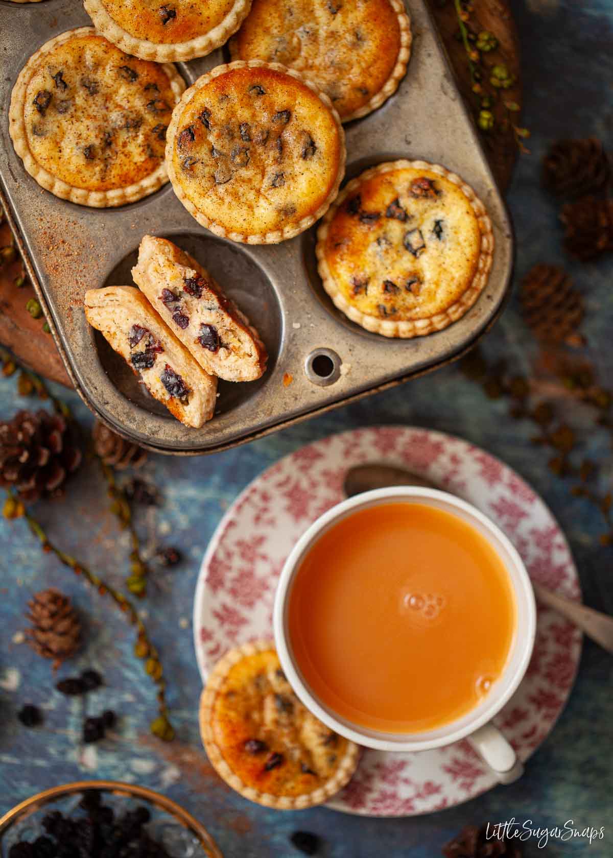Pastry cheesecakes in a baking tin with a cup of tea. One is cut in half revealing the filling.