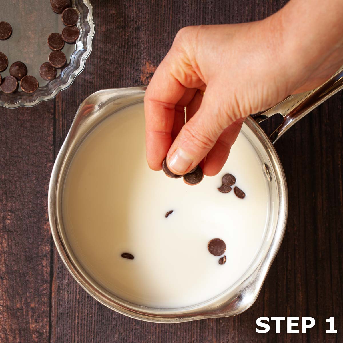 A person adding chocolate chips to milk in a saucepan.