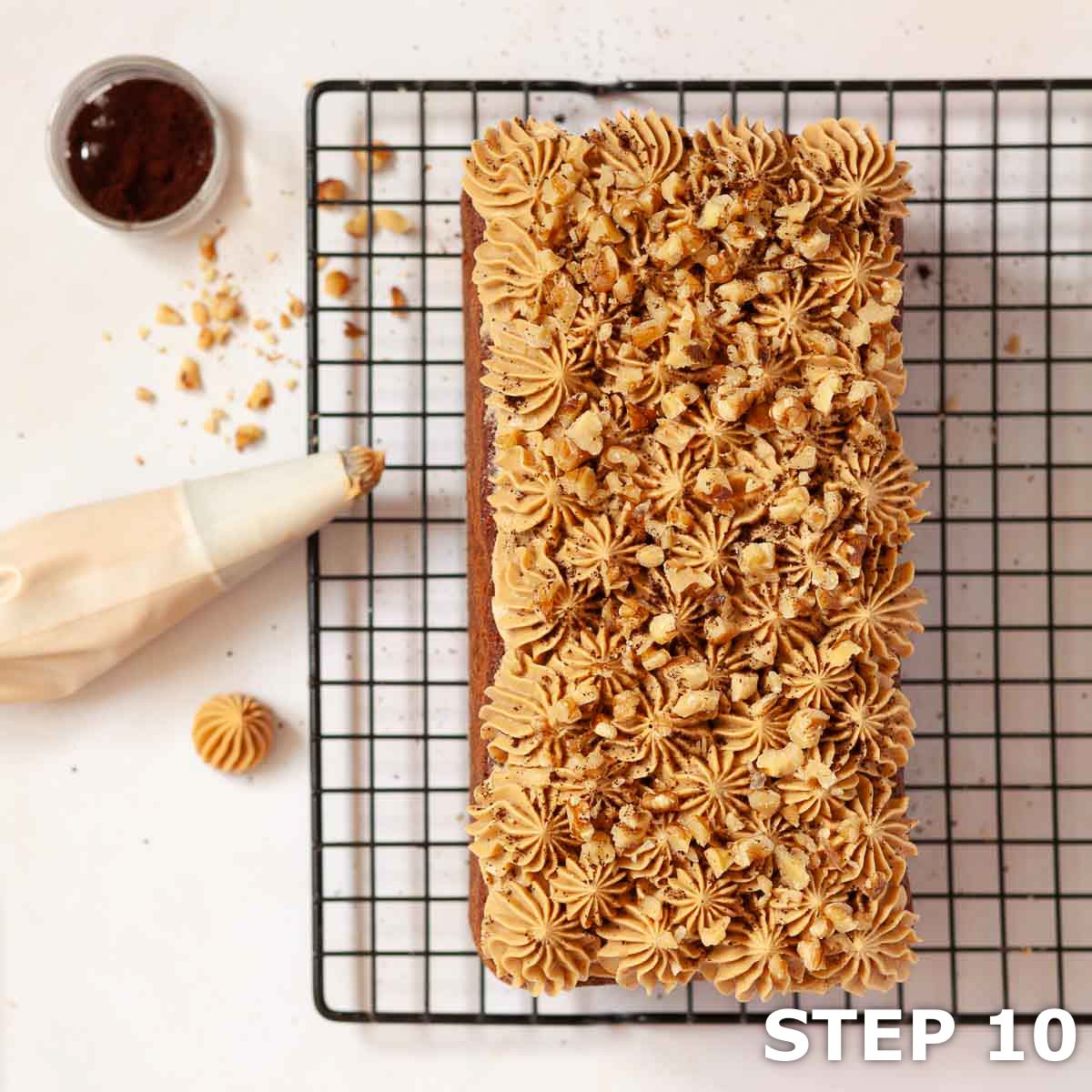 Coffee cake on a wire rack with buttercream on the top and the piping bag next o it.