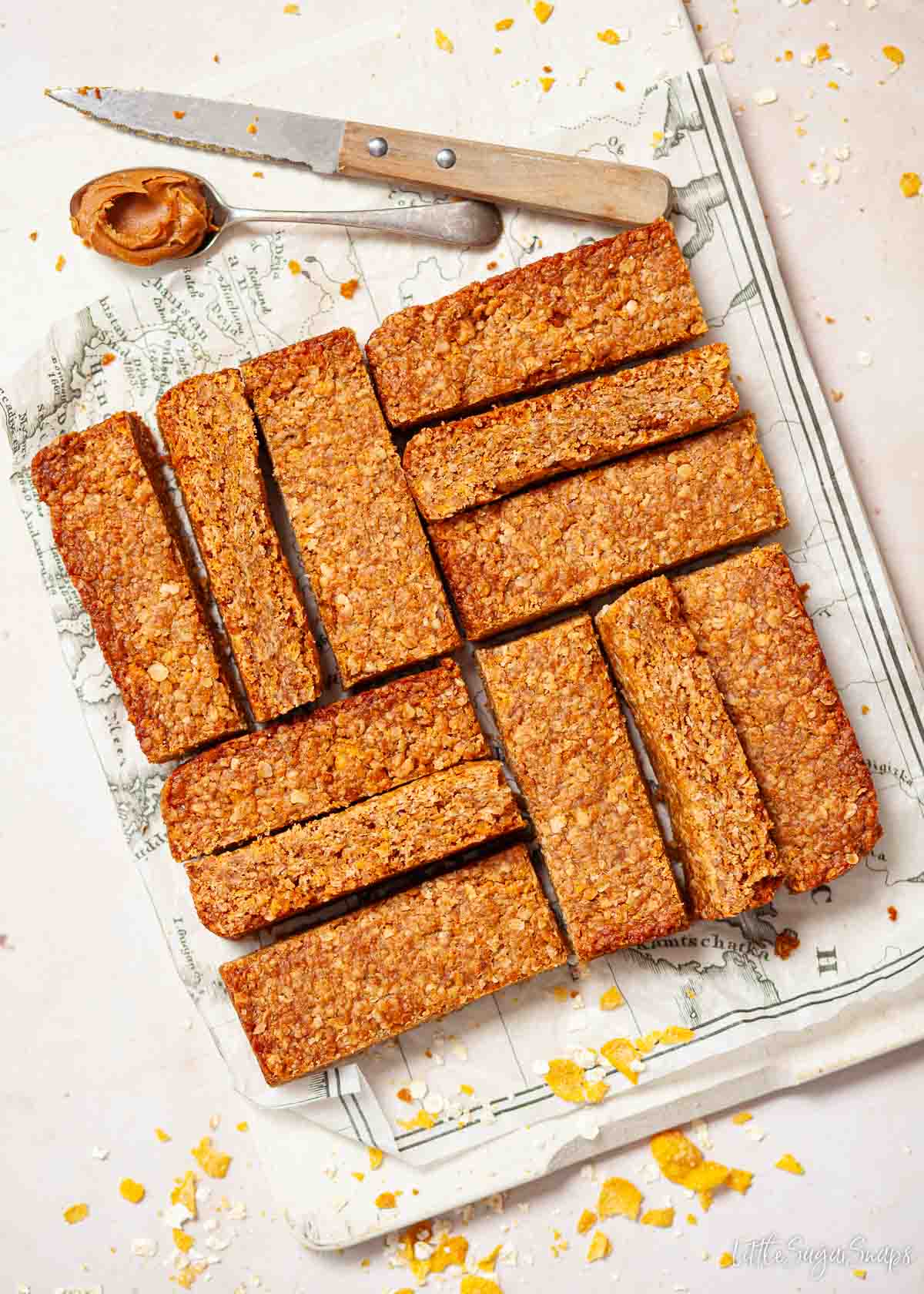 Cornflake traybake slices on a board with a knife and a teaspoon holding Biscoff spread.