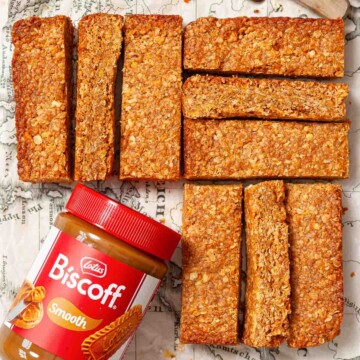 Slice of cornflake flapjack on a board with a jar of Biscoff spread alongside them.