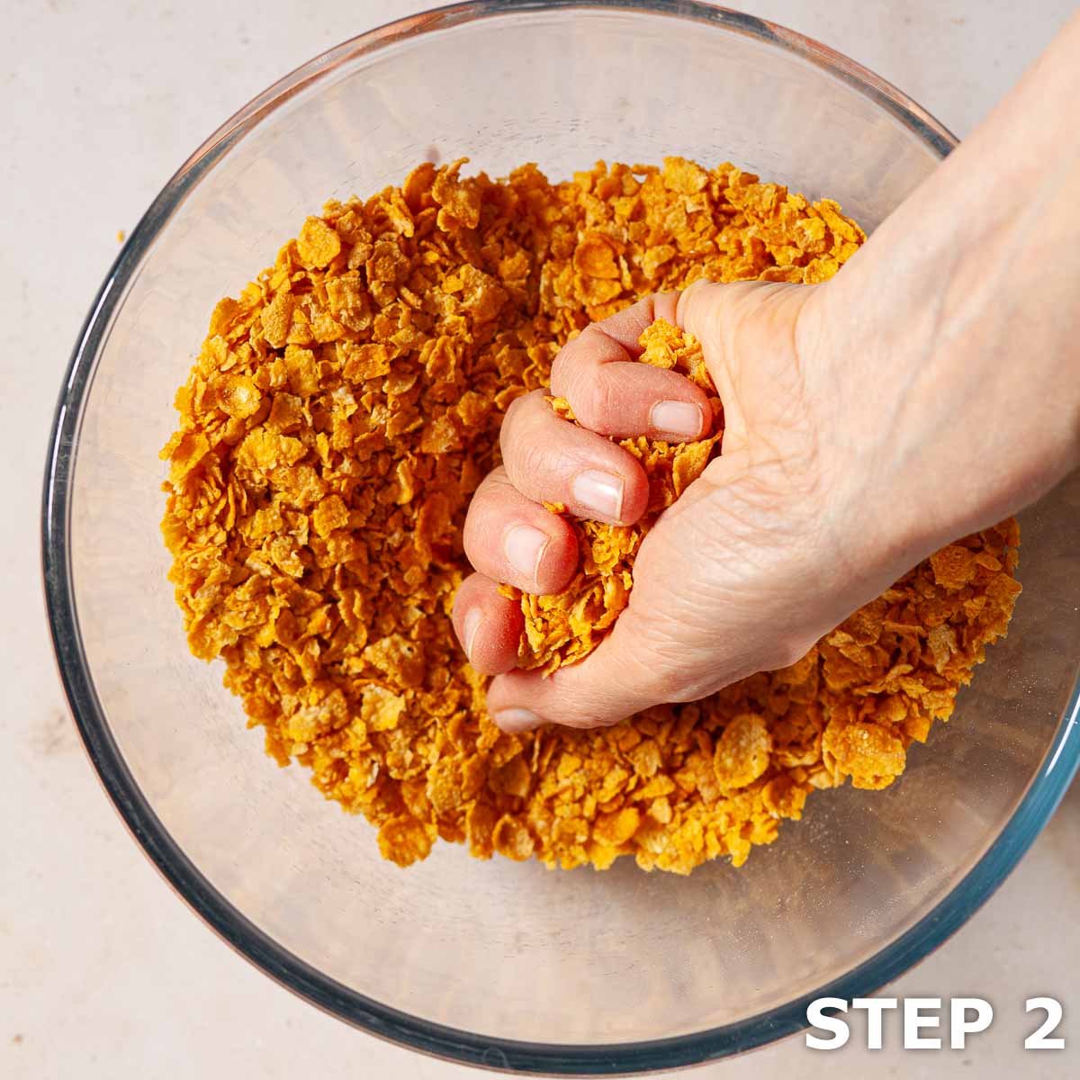 A person crushing Cornflakes cereal in a pyrex bowl.