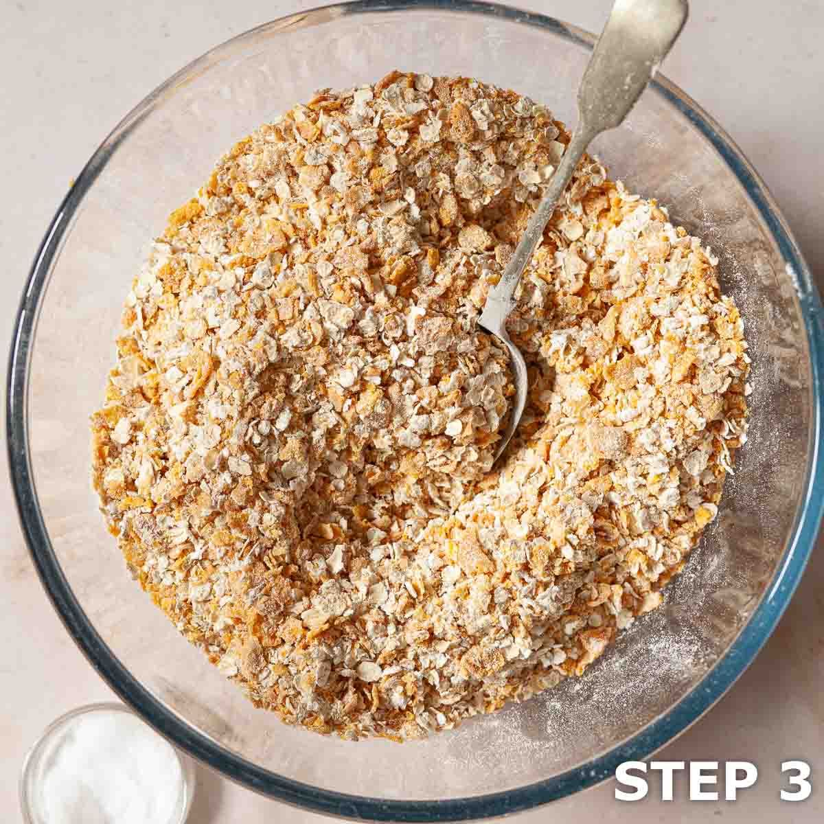 Crushed cornflakes, roled oats ans flour stirred together in a mixing bowl with a spoon.
