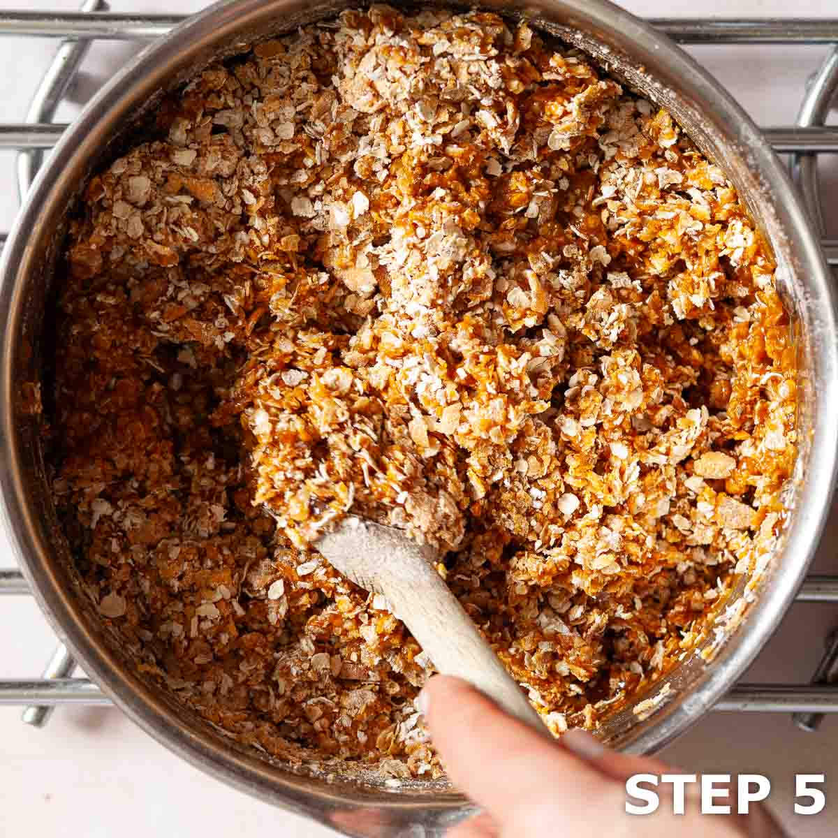 A person mixing crushed cornflakes, oats and flour into liquid ingredients for flapjack.