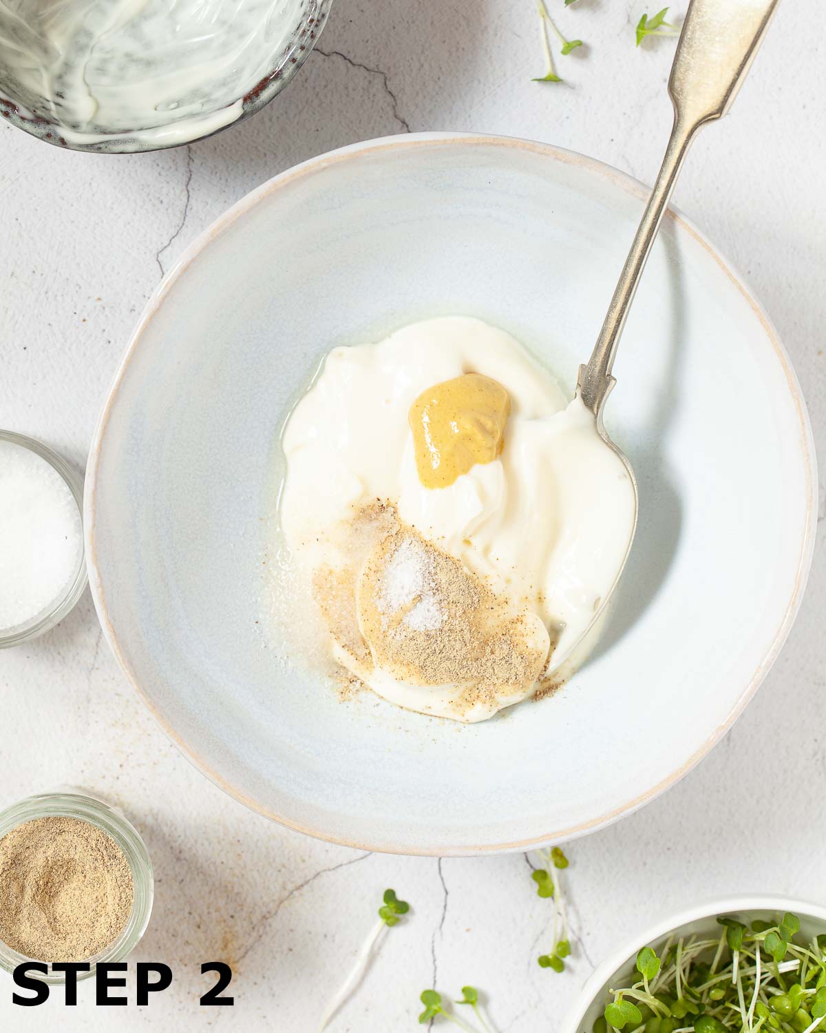 A bowl of mayonnaise, dijon mustard and seasoning in a bowl with a spoon in it.