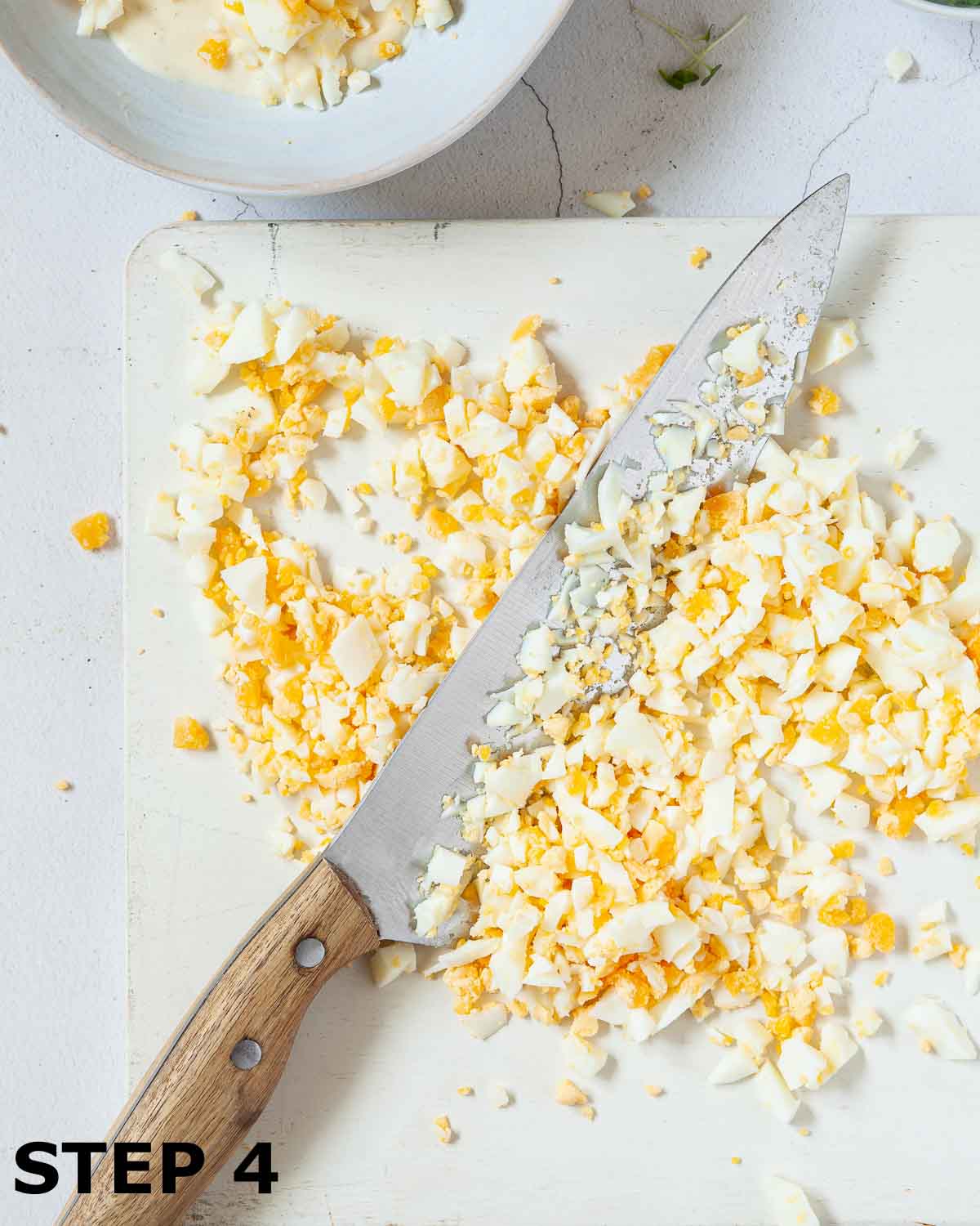 Hard boiled eggs being chopped with a large knife on a chopping board.