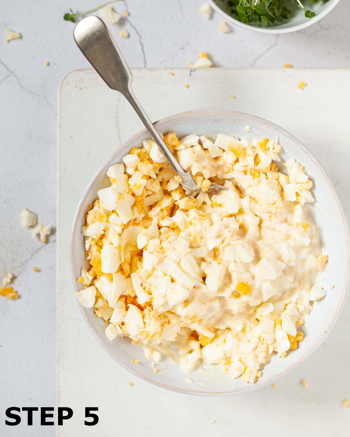 Chopped eggs being mixed into a mayonnaise dressing in a bowl.