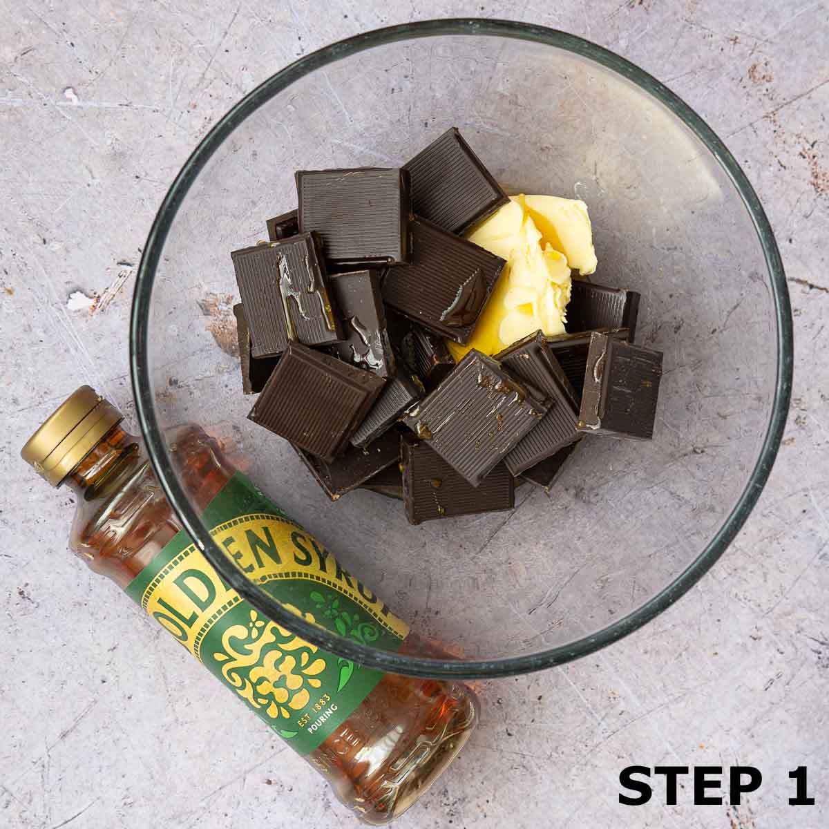 Butter, chocolate and syrup in a mixing bowl with a bottle of golden syrup next to it.