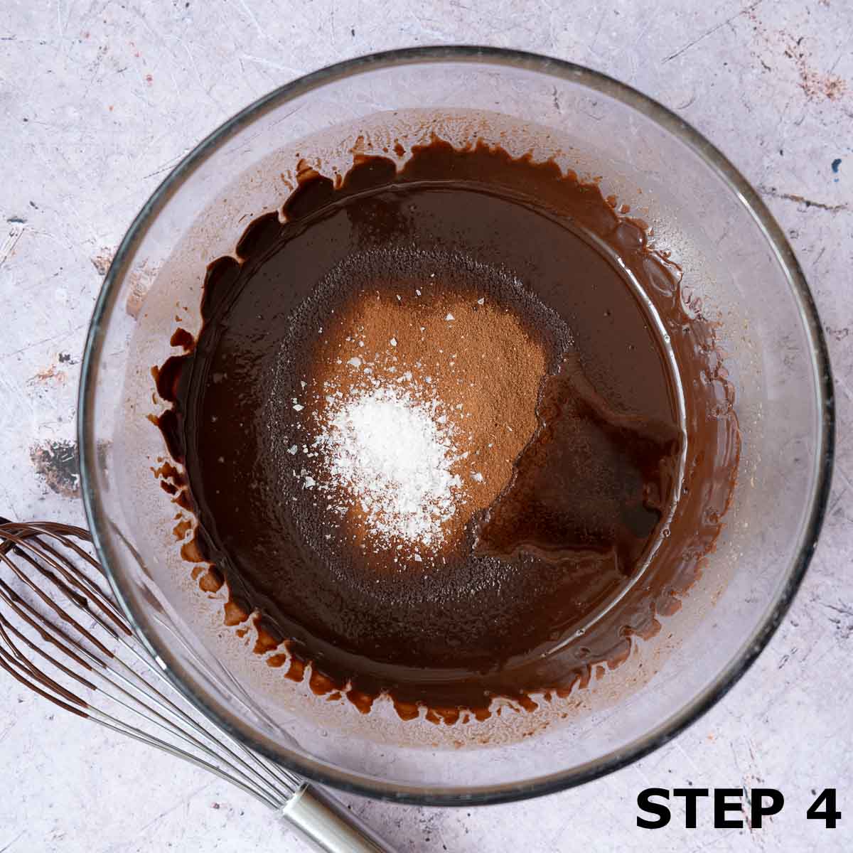 Melted chocolate mixture with cocoa powder and sea salt flakes about to be mixed in with a whisk.
