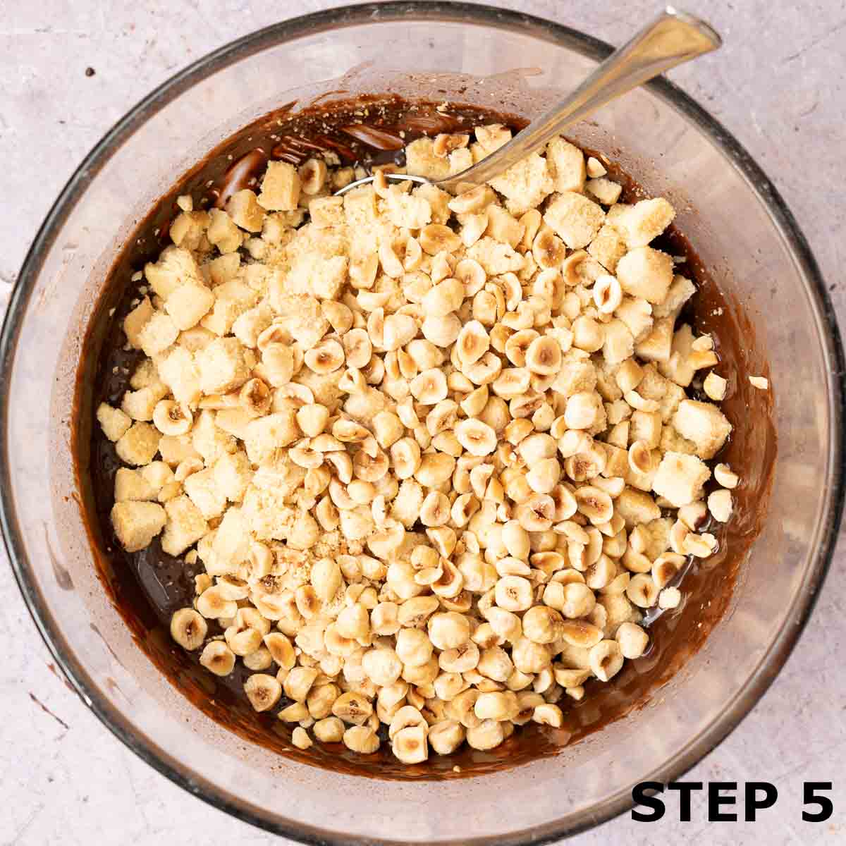 Chopped shortbread and chopped roasted hazenuts in a bowl with chocolate tiffin mixture.