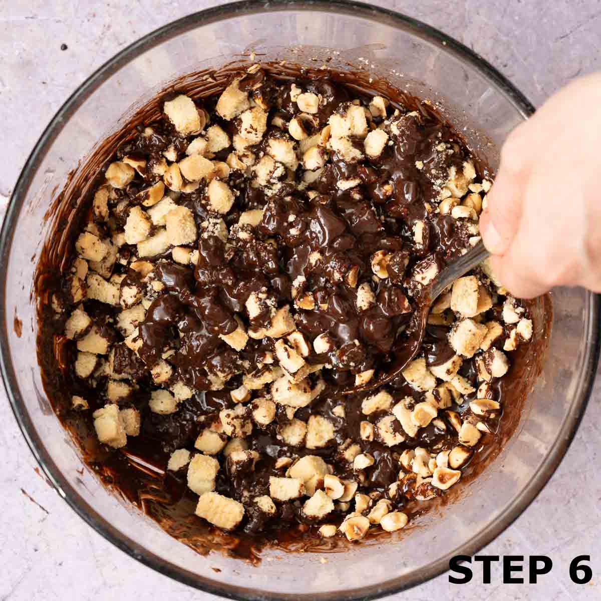 A person stirring biscuits and nuts into tiffin cake mixture.
