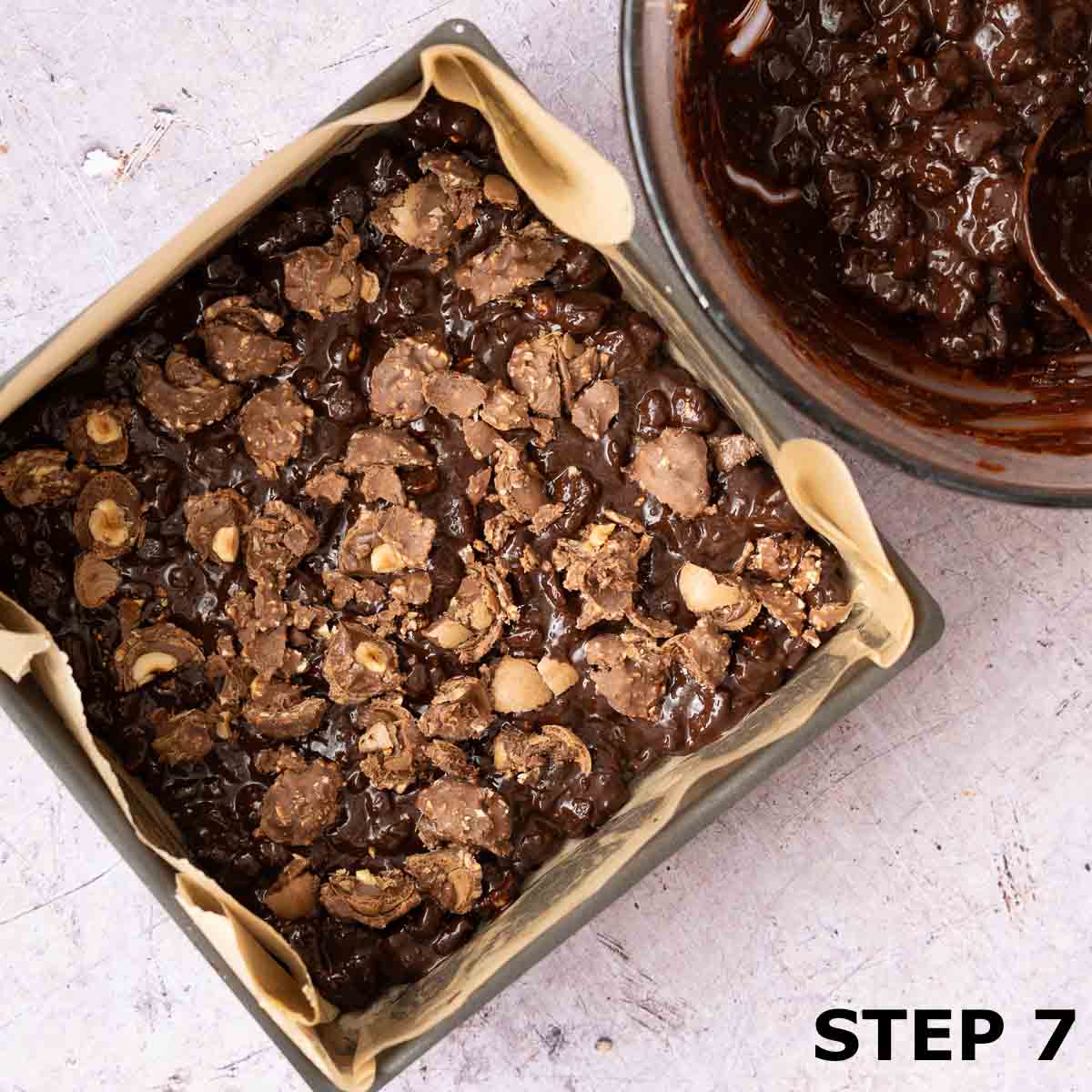 Tiffin mixture in a lined baking tin with a layer of chopped chocolates on top.