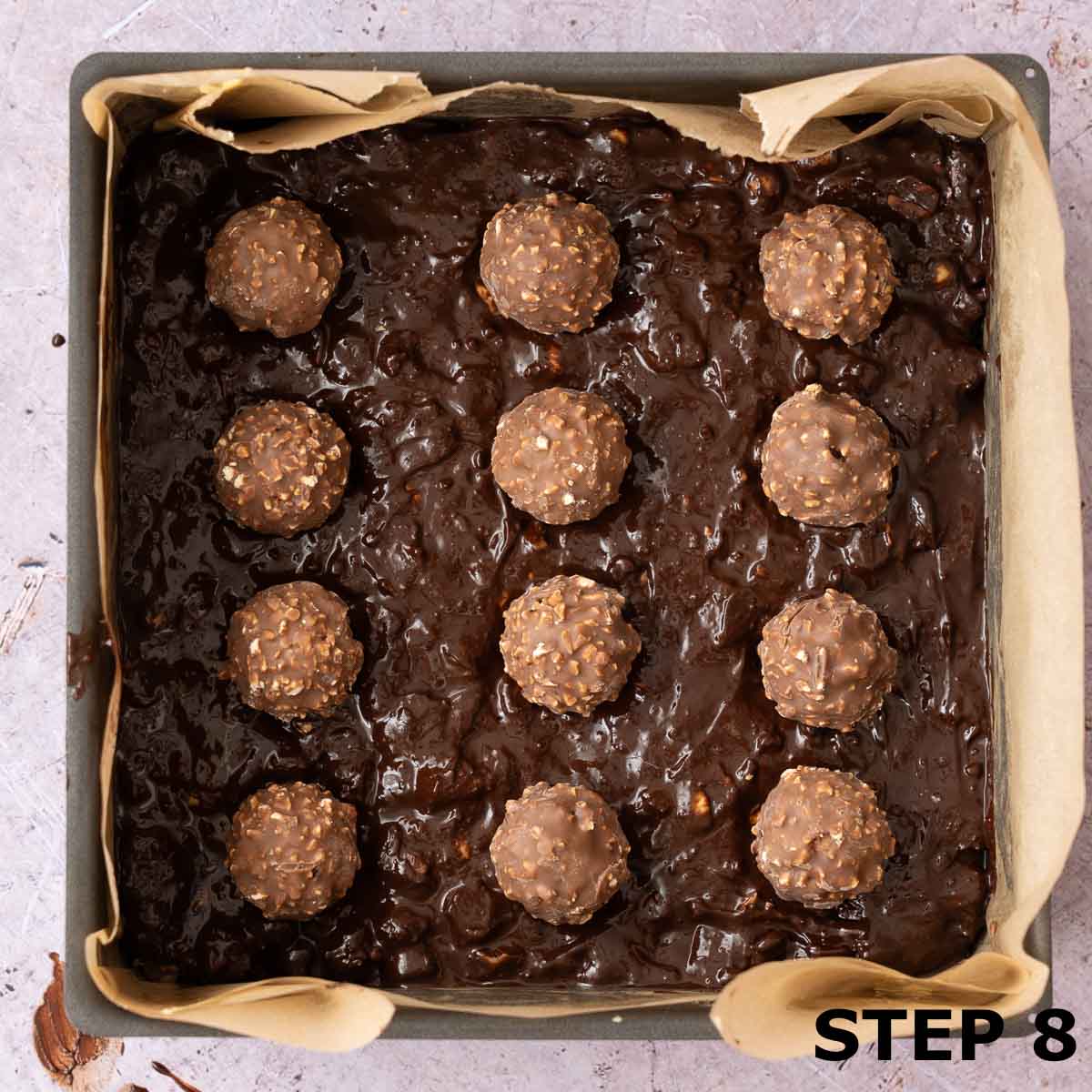 Chocolate hazelnut tiffin cake mixture in a baking tin with Ferrero Rocher chocolates pressed into it.