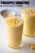Two glasses of ginger pineapple smoothie without banana topped with coconut with text overlay.