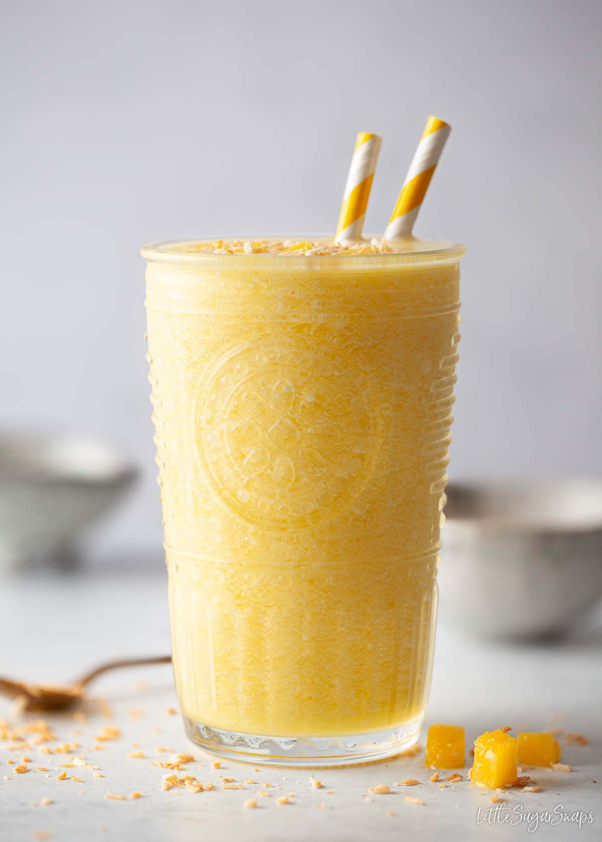 A glass of ginger and pineapple smoothie with 2 striped straws in it.