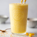 A glass of ginger and pineapple smoothie with straws in it.