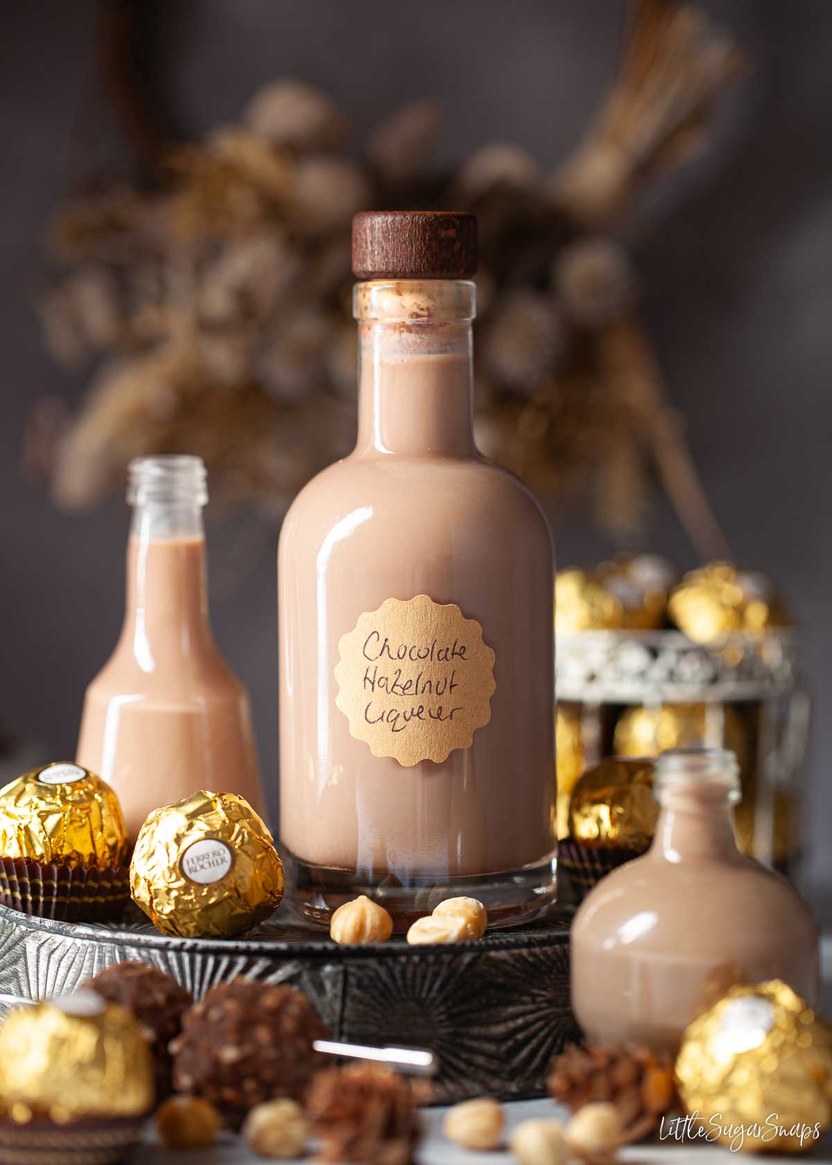 A bottle of labelled chocolate hazelnut liqueur surrounded by smaller bottles and Ferrero Rocher chocolates.