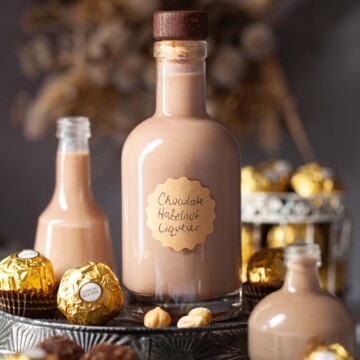 A bottle of labelled chocolate hazelnut liqueur surrounded by smaller bottles and Ferrero Rocher chocolates.