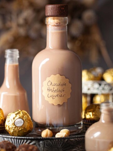 A bottle of labelled chocolate hazelnut liqueur surrounded by smaller bottles and Ferrero Rocher chocolates.