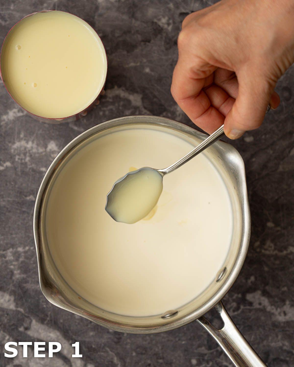A person adding condensed milk to a pan of cream.