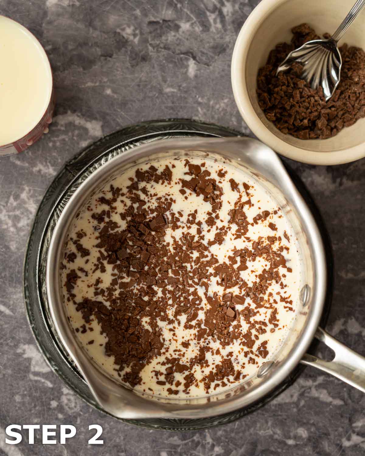Chopped chocolate sprinkled over warm cream in a saucepan.